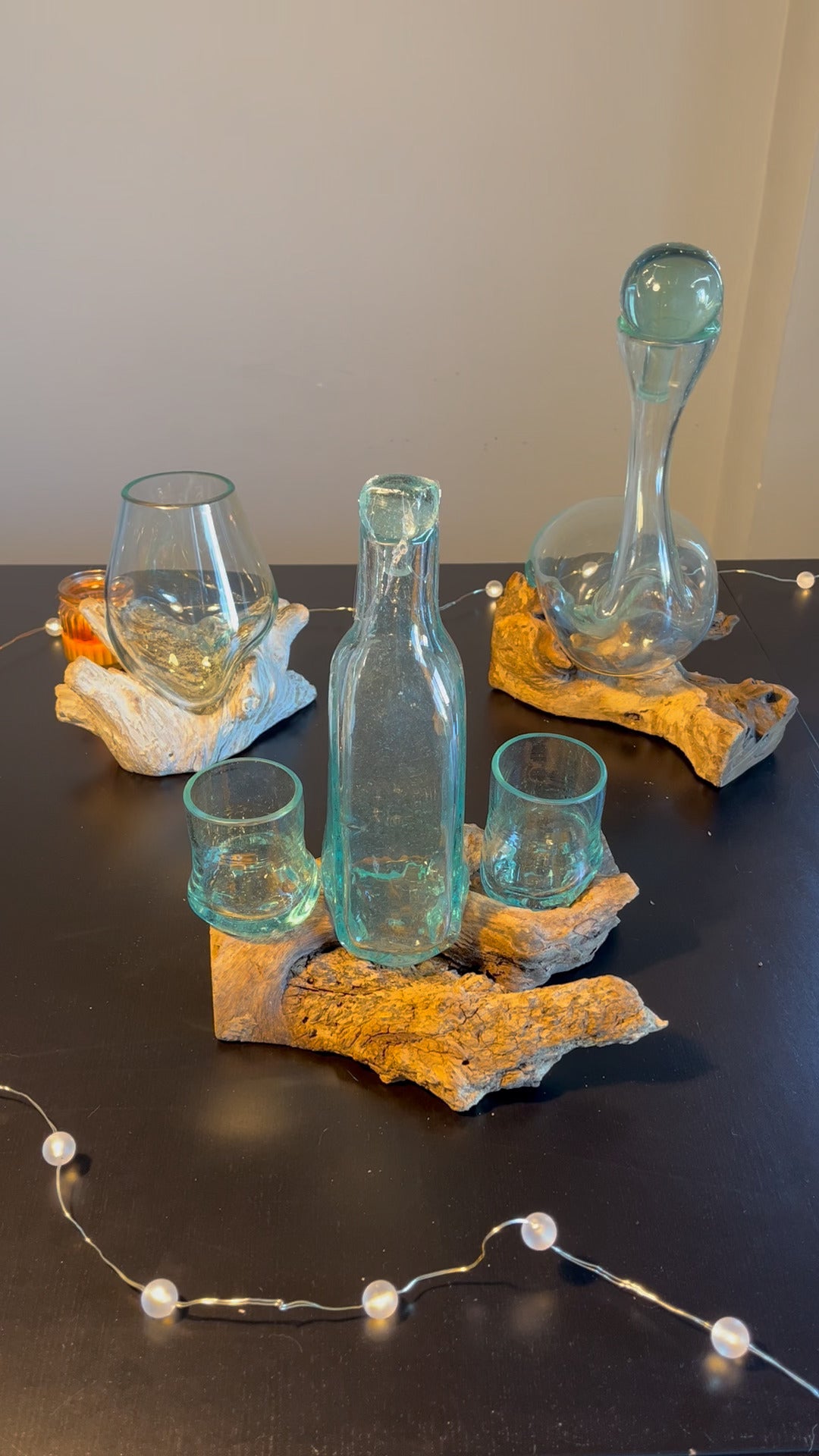 Obiecte decorative artizanale din sticla turnata pe lemn exotic. Aceste seturi de sticla si lemn sunt asezate pe o masa si inconjurate de becutele aprinse.